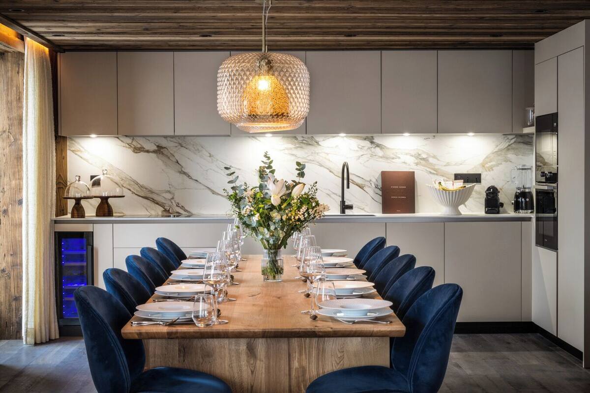 A modern dining area with a marble backsplash, a wooden dining table set for six, and a hanging light fixture.