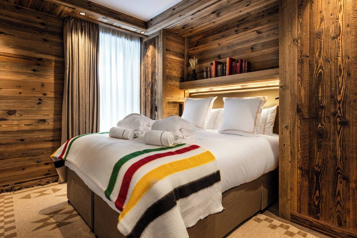 A wooden-paneled room with a bed, a bookshelf, and a window with curtains.