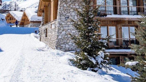 A snow-covered mountain lodge with stone and wood construction, large windows, and a balcony. - Silverstone by Alpine Resorts (Val-d'Isere)
