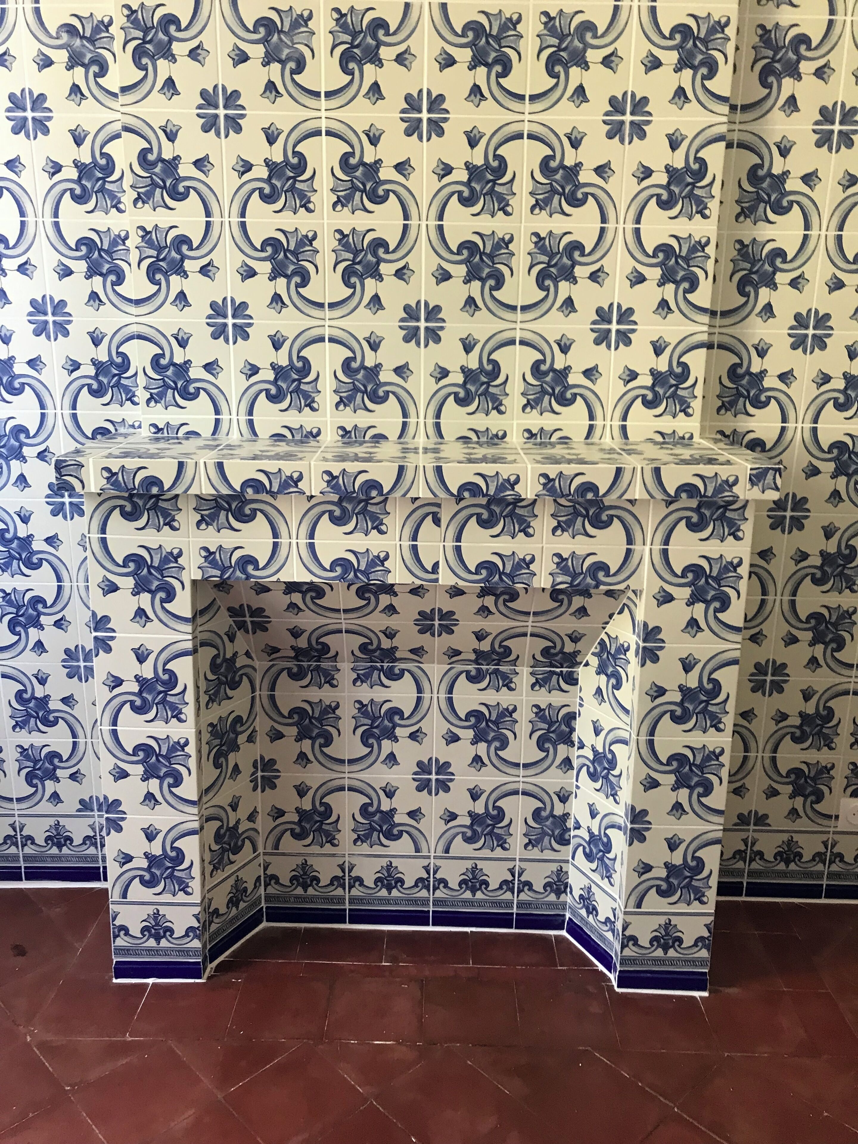 A tiled wall with a decorative pattern and a corner shelf.