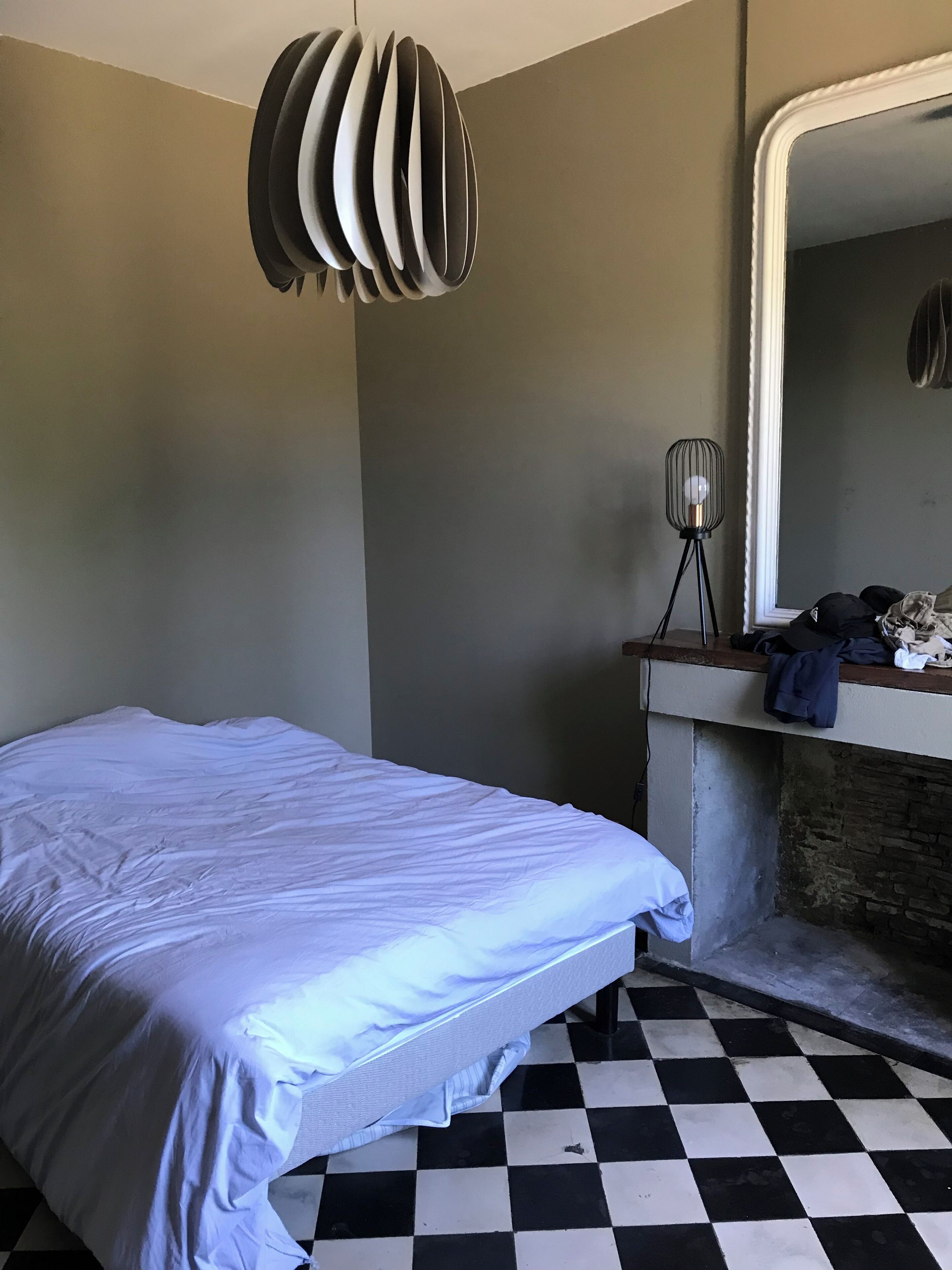 A room with a bed, a checkered floor, a mirror, and a lamp.