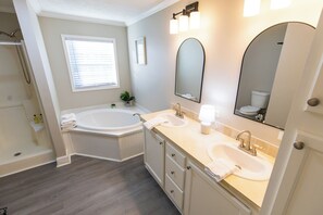 A modern bathroom with a bathtub, two sinks, a large mirror, and a shower area. - Hendrix Hideaway (Lexington)