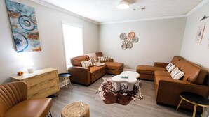 Ein Wohnzimmer mit Ecksofa, einem kleinen runden Tisch, einem Holzschrank und einem Kuhfellteppich.