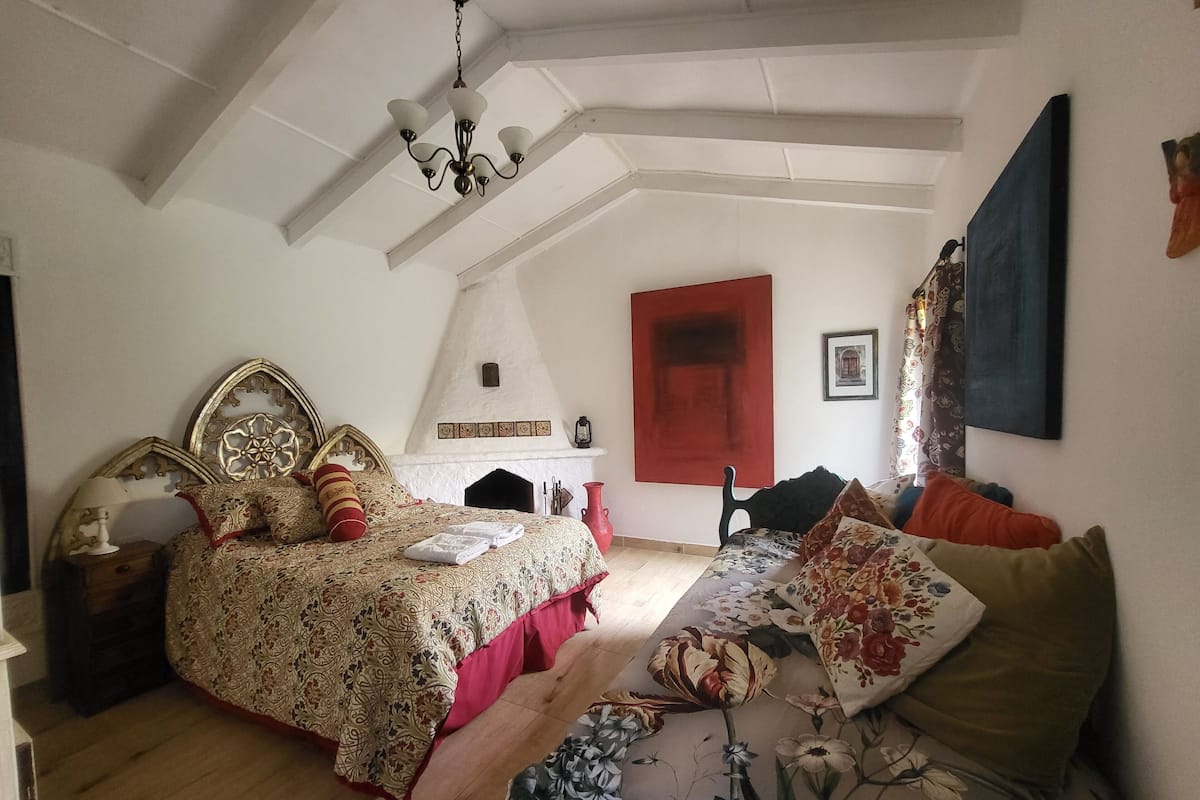 A bedroom with a large bed, a sofa, a fireplace, and a ceiling fan.
