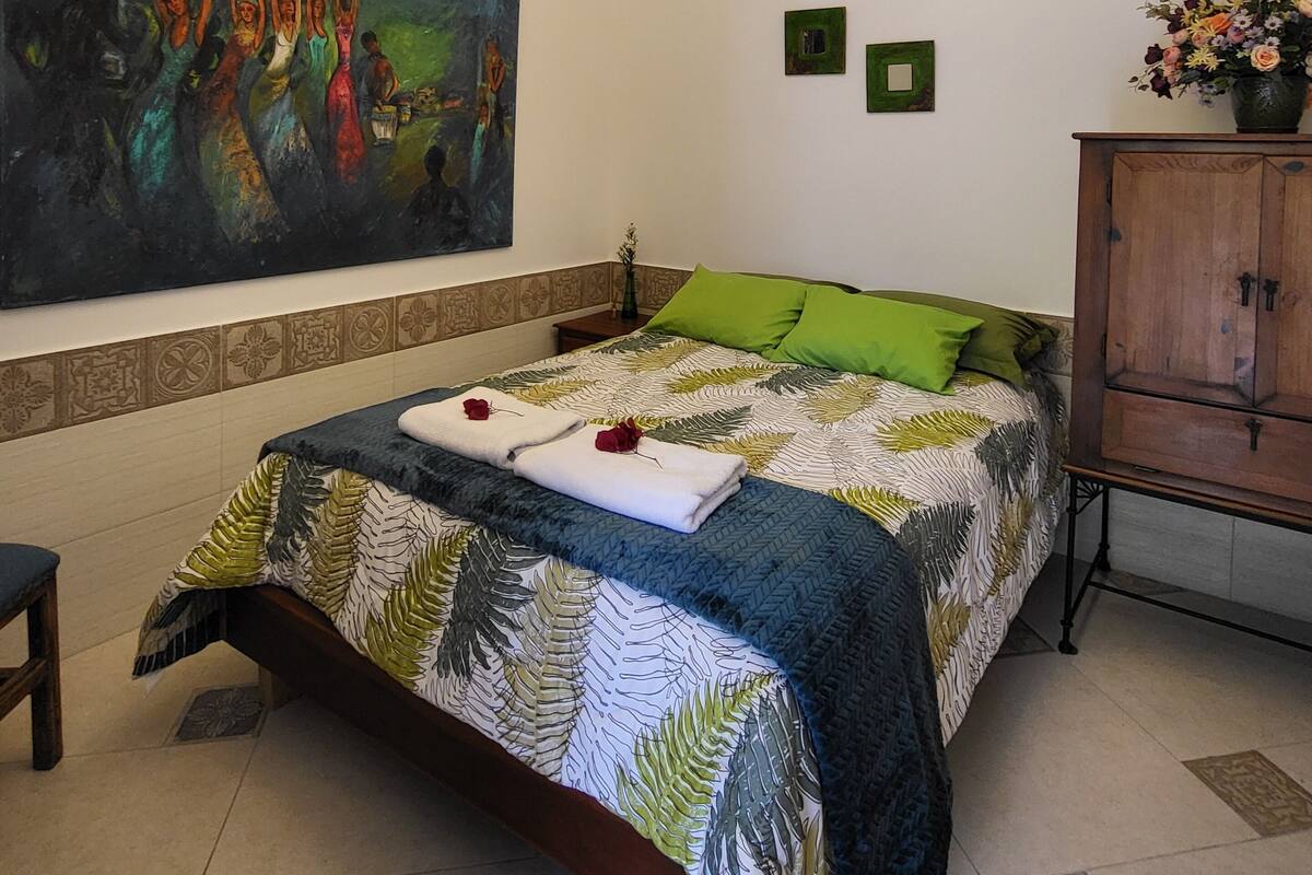 A bedroom with a bed, a painting, a chandelier, and a cabinet.