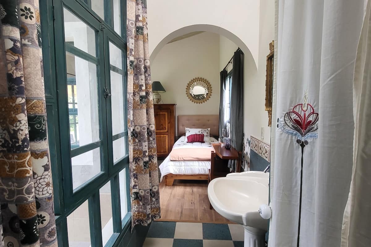 A bedroom with a bed, a bedside table, a mirror, and a window.