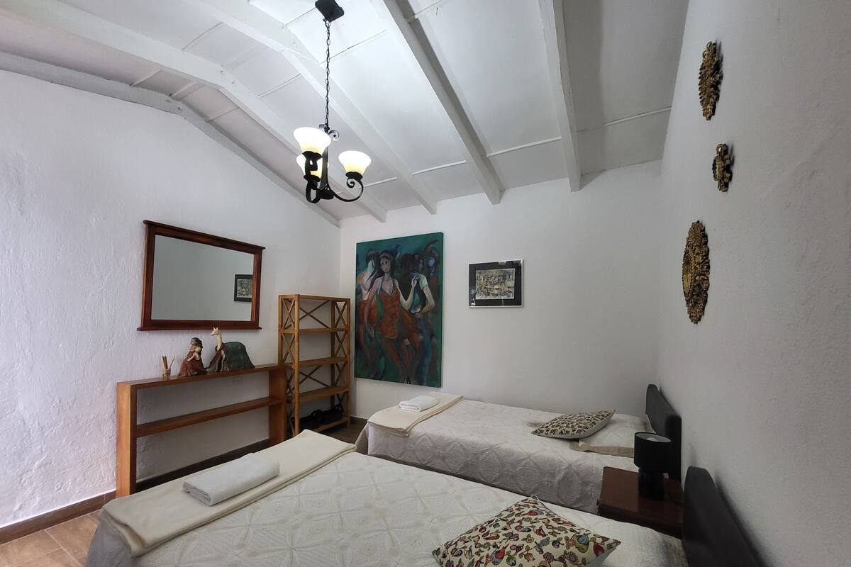 A bedroom with two beds, a wooden shelf, a painting, and a chandelier.