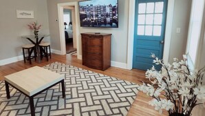 A living room with a ceiling fan, a television mounted on the wall, a blue door, and a patterned rug. - Balcony Vibes and Blue Skies (Montgomery)