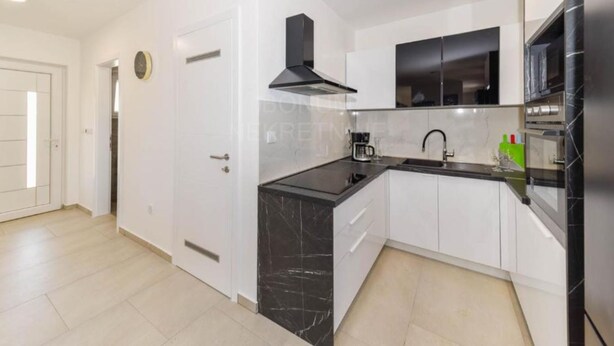 Una cocina moderna con armarios blancos, encimeras negras y una campana extractora negra.