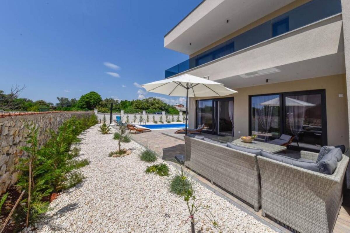 Ein modernes Haus mit Swimmingpool, Sitzgelegenheiten im Freien und einer Steinmauer.