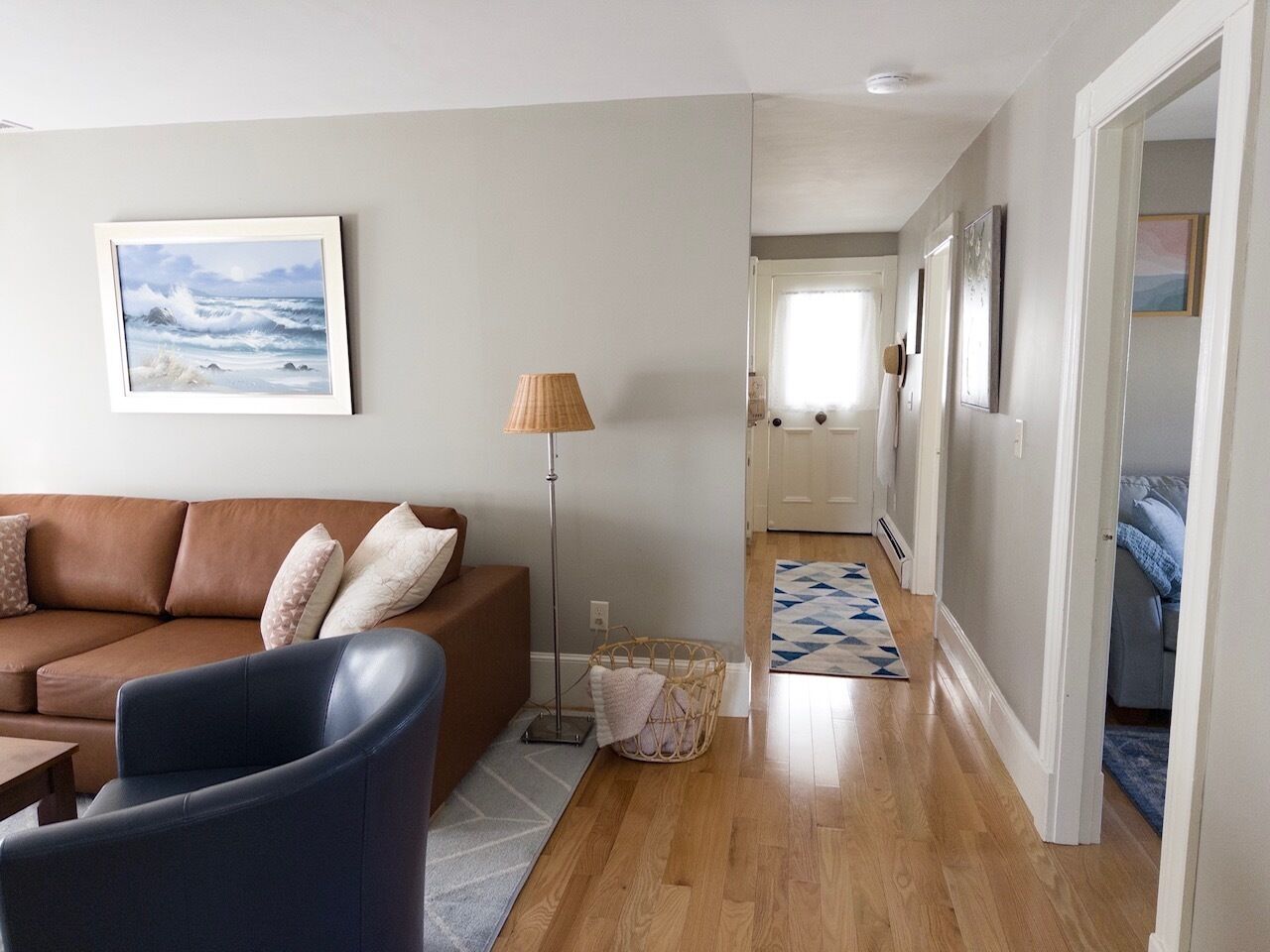 A living room with a brown sofa, a blue armchair, a floor lamp, and a framed painting on the wall.
