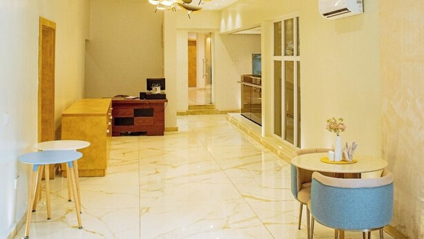 A hotel lobby with a marble floor, a reception desk, a blue chair, and pendant lighting.