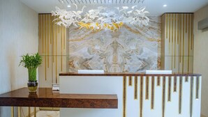 A reception desk with a marble wall and gold accents, a hanging light fixture, and a potted plant.