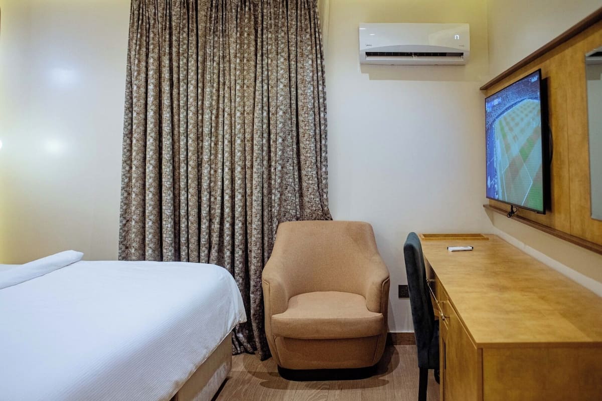 A hotel room with a bed, a chair, a desk, an air conditioner, and a television.