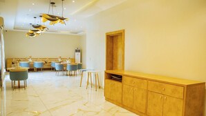 A spacious room with a marble floor, a wooden cabinet, a dining area with blue chairs, and a modern chandelier.
