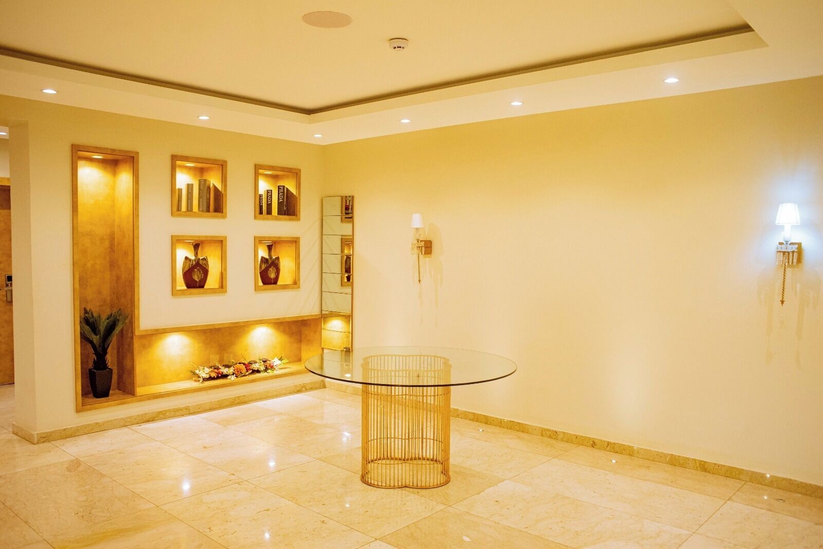 Un vestíbulo moderno con una mesa de vidrio, jarrones decorativos e iluminación en la pared.