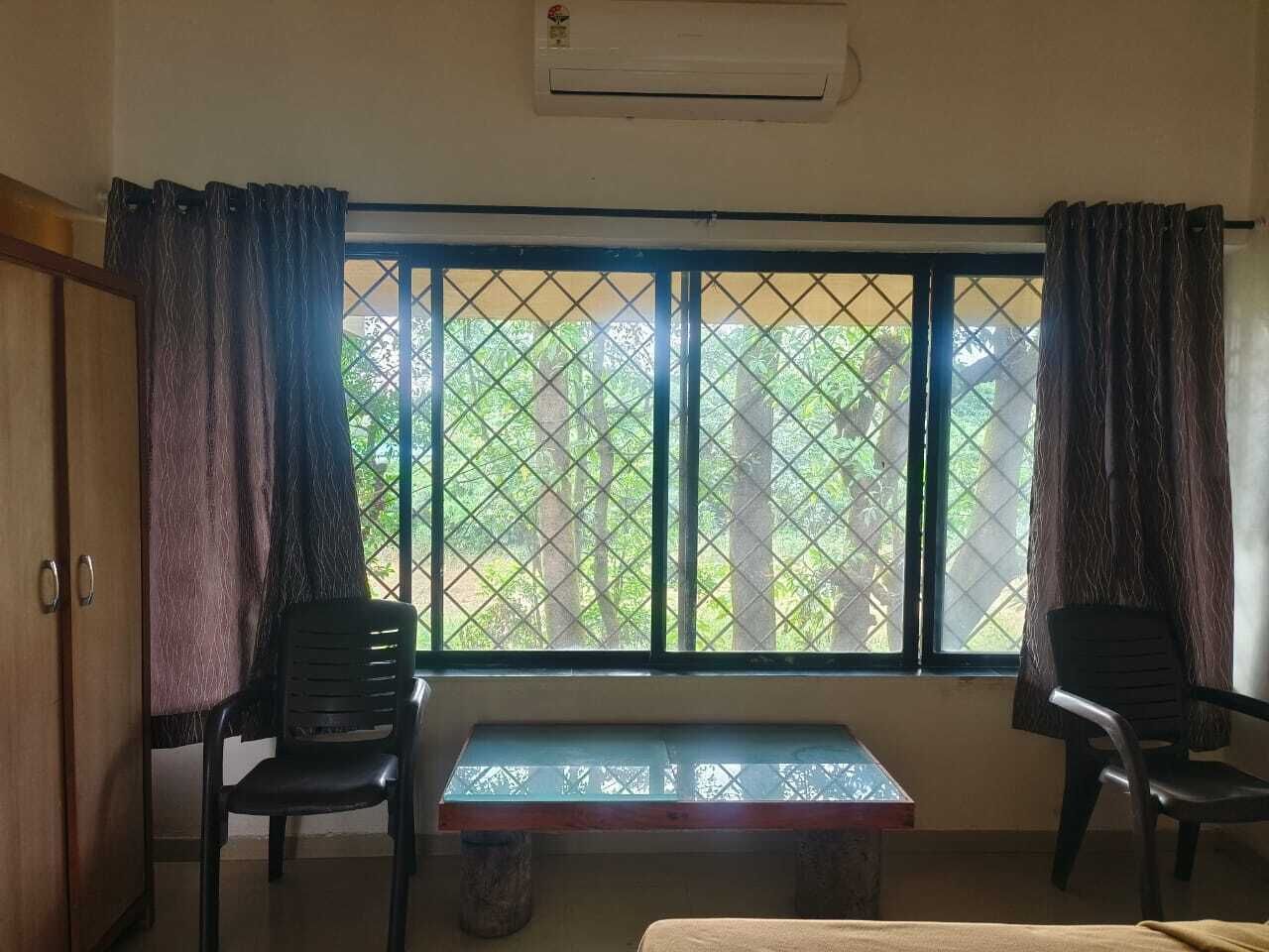 A room with a window, two chairs, a small table, and an air conditioning unit.