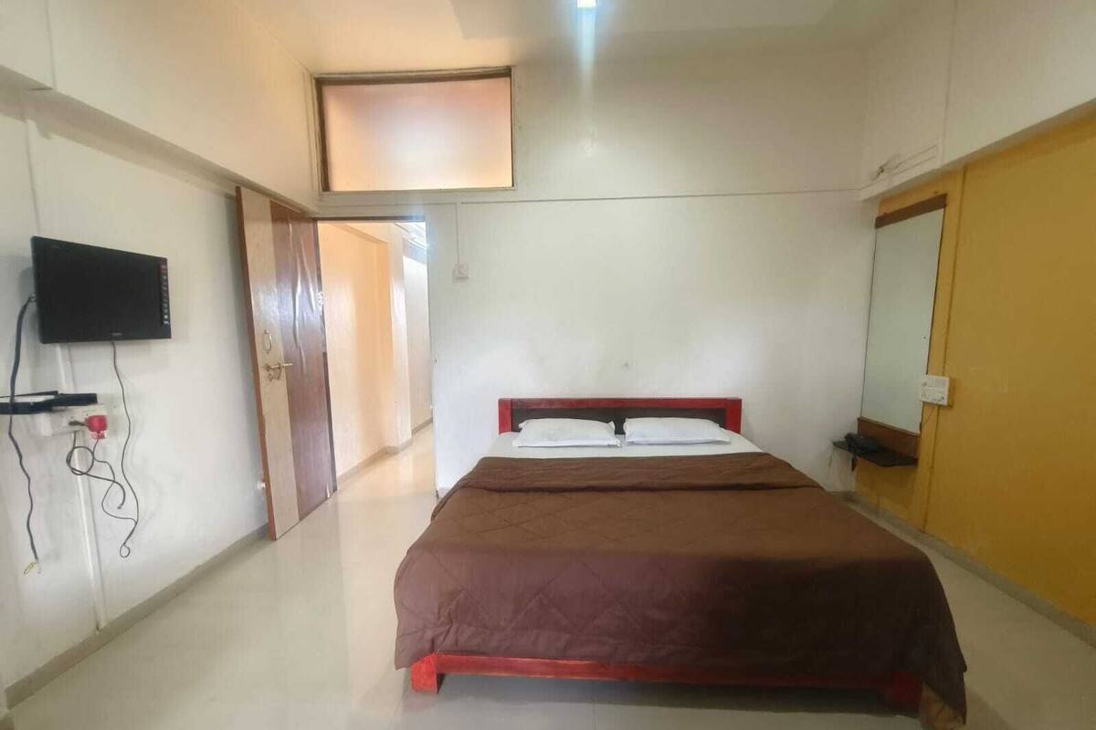 A bedroom with a bed, a television mounted on the wall, and a door leading to another room.