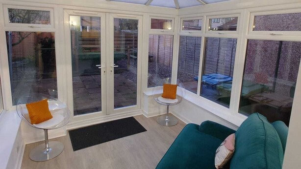 A conservatory with a glass ceiling, white-framed windows, a green sofa, two small tables with chairs, and a lamp. - RF-Entire House -Central Scotland-Falkirk| Self-Check-in |Pet-friendly | Parking (Falkirk)