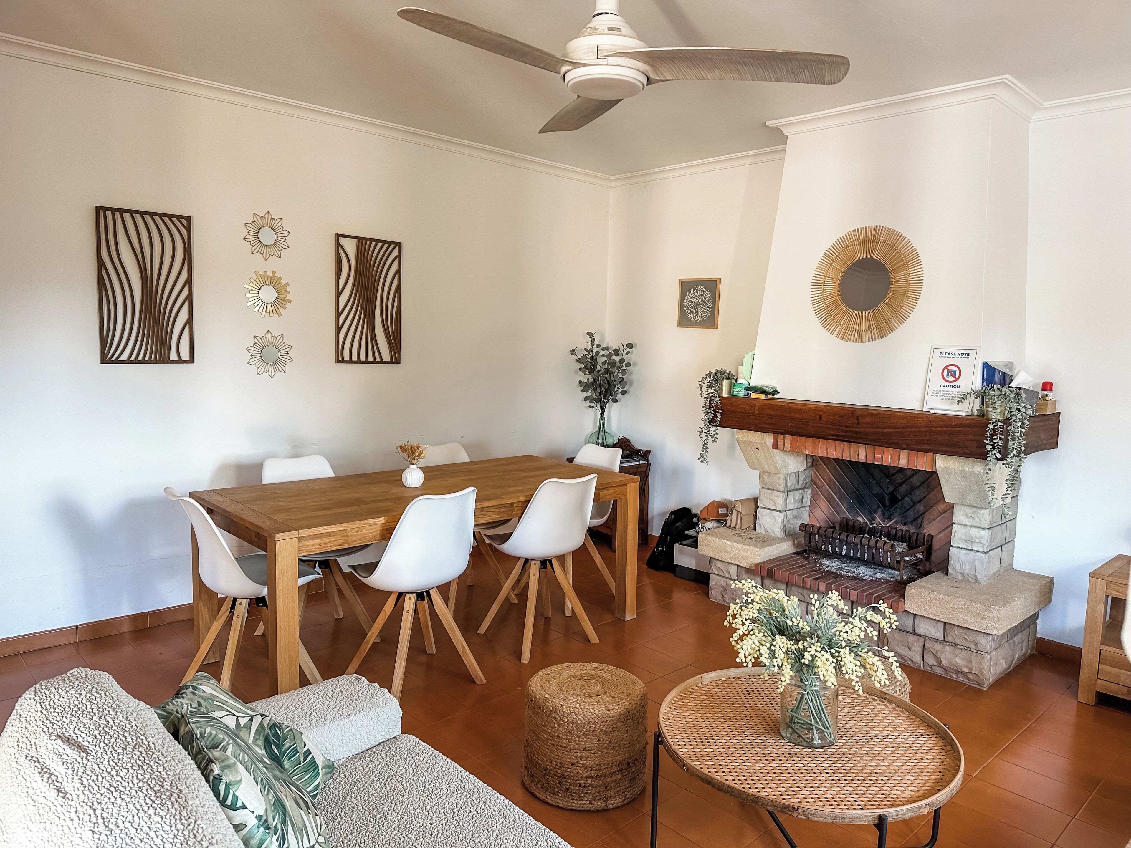 A dining area with a wooden table and white chairs, a fireplace with a stone mantle, and a ceiling fan.
