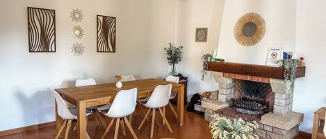 A dining area with a wooden table and white chairs, a fireplace with a stone mantle, and a ceiling fan.