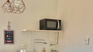 Et køkken med en hvid bordplade, en stålvask, en sort mikroovn på en hylde og en hængende lampe.