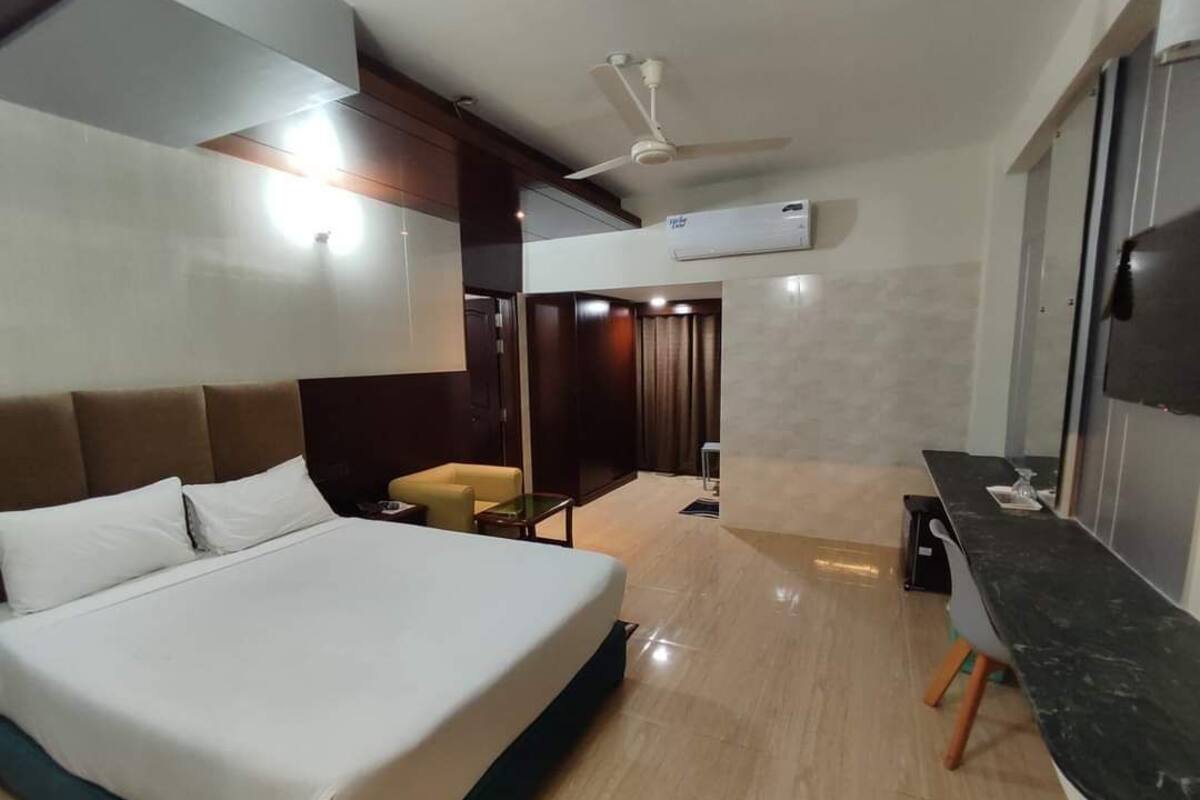 Habitación de hotel con cama, escritorio, silla, ventilador de techo, unidad de aire acondicionado y televisor.