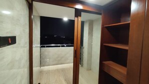 A room with a sliding glass door leading to a balcony, a wooden shelf unit, and a light switch on the wall. - Media International CoxsBazar  (Cox's Bazar)