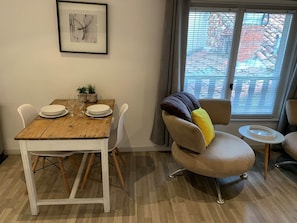 A dining area with a wooden table, white chairs, a cushioned armchair, and a small side table. - Studio 1*, impasse de la Chantrerie, floor 3 (Cahors)
