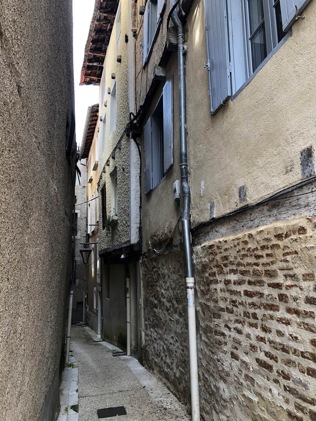 Une ruelle étroite bordée de bâtiments des deux côtés, avec des murs en briques apparentes et un chemin pavé.