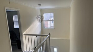 Interior com vários níveis, incluindo uma escada, luminária pendente e uma janela com persianas.