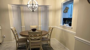 Uma sala de jantar com uma mesa redonda, quatro cadeiras, um candelabro e uma janela que dá para a cozinha.