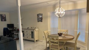 Uma sala de jantar com uma mesa redonda, cadeiras, um candelabro e uma mesa posta com uma tigela e pratos.