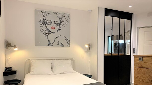 A modern bedroom with a bed, bedside tables, a nightstand, a lamp, a dresser, and a wall art piece.