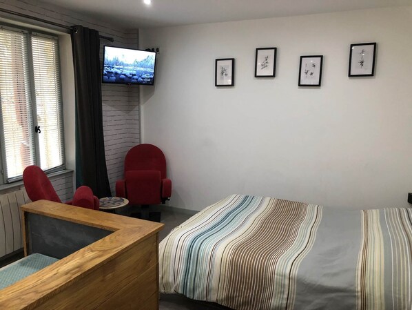 A room with a bed, a red chair, a TV mounted on the wall, and framed pictures on the wall. - Studio 1*, Impasse de la Chantrerie, 1st floor (Cahors)