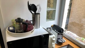 A kitchen with a microwave, kettle, coffee maker, and utensils on the counter.