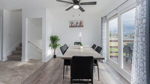 A dining area with a large table, chairs, a ceiling fan, a potted plant, and a view through large windows. - Pondside Retreat 4BR w/ Hot Tub & Pool Table & BBQ (Hilliard)