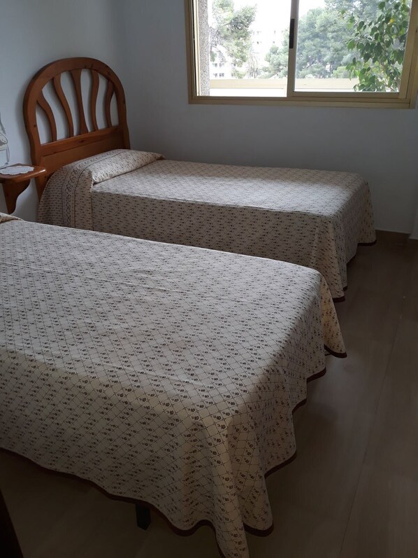 A room with two single beds, a wooden headboard, a small bedside table, and a window with a view of trees. - NEAR THE SEA AND THE ADVENTURE PORT, WITH AIR CONDITIONING AND FREE WIFI (Salou)