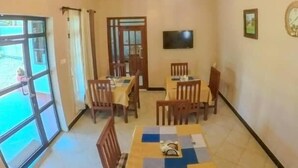 Un comedor con una mesa preparada para cuatro personas, un televisor montado en la pared y un ventanal con cortinas.