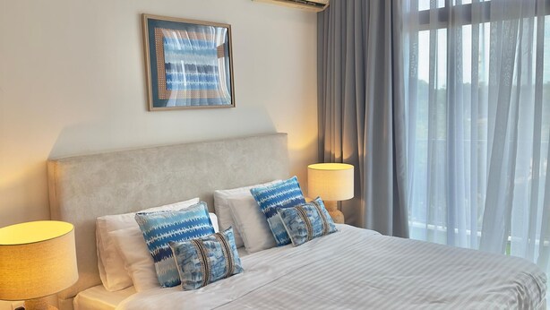 Habitación de hotel con una cama grande, dos lámparas de noche, aire acondicionado en la pared y una ventana con cortinas translúcidas.