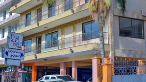 Un hotel de varios pisos con balcones, una palmera y coches estacionados.
