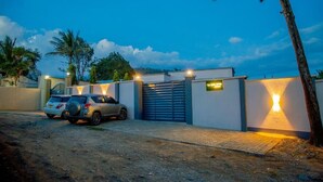 Zona residencial cerrada al anochecer con dos autos estacionados, un camino pavimentado y una entrada bien iluminada.