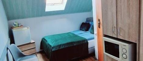 Una habitación pequeña con cama, escritorio, silla, mesita, radiador y armario.
