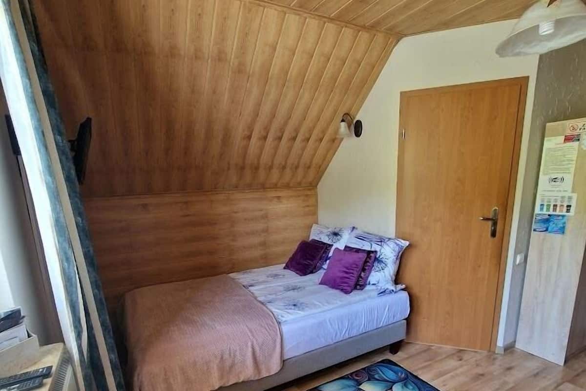 A cozy bedroom with a sloped ceiling, a bed with a colorful floral rug, and a wooden door.