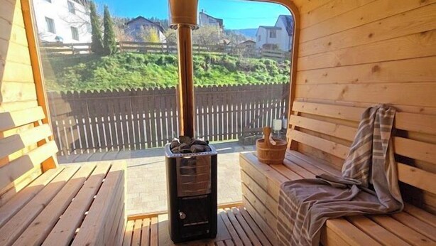 A wooden sauna with a bench and a bench seat, a sauna heater, and a view of a wooden fence and houses. - Pokoje Gościnne Kacper blisko Gondoli (Szczyrk)