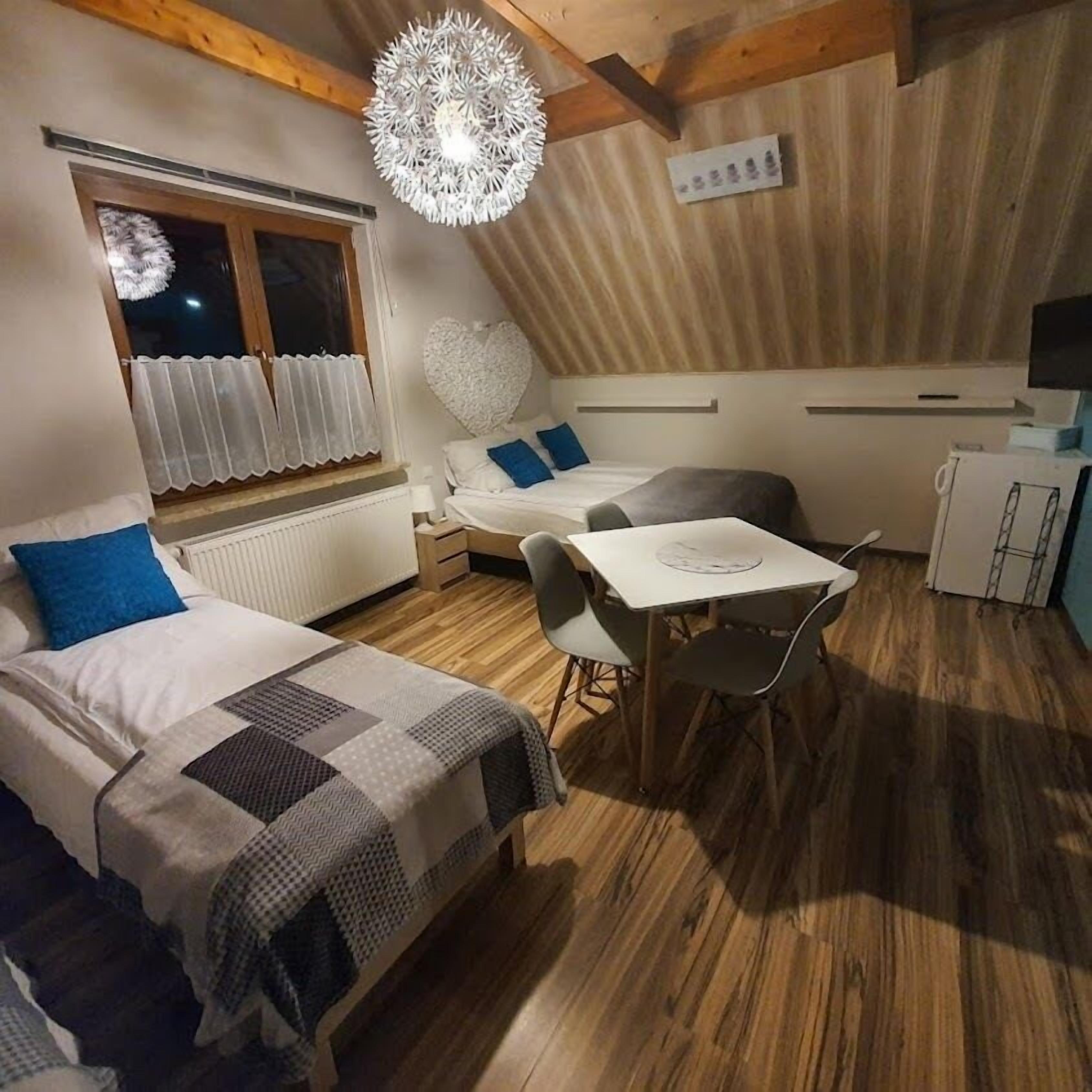 A cozy room with two beds, a dining table, and a ceiling light fixture.