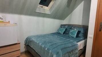 A compact bedroom with a single bed, a small desk, and a window.