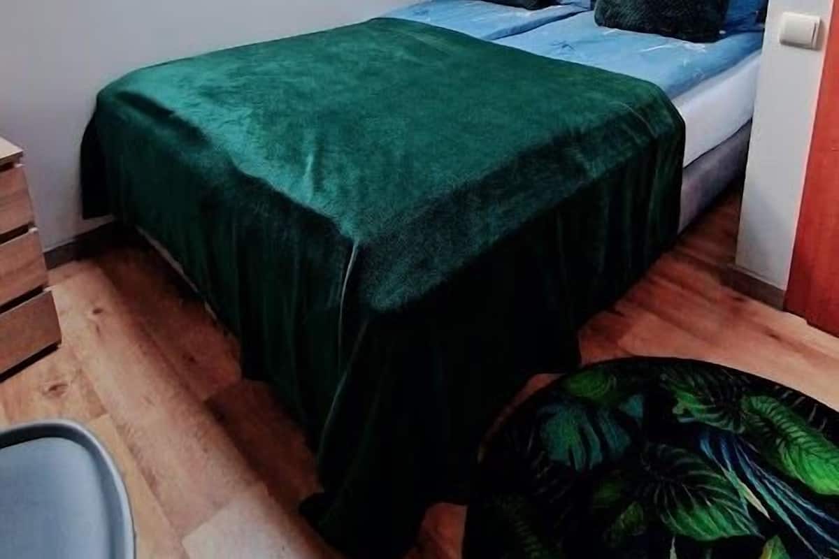 A small, cozy bedroom with a sloped ceiling and skylight, a bed with a green bedspread, and a small round table with a chair.