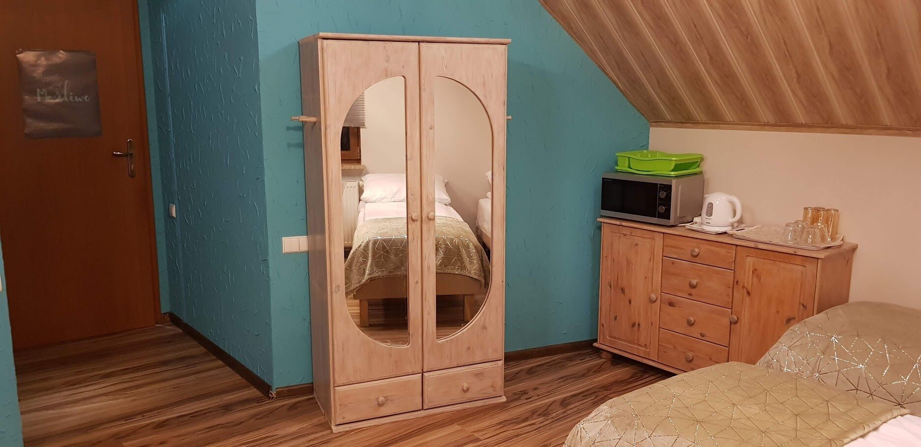 A bedroom with a wooden wardrobe, a bed, a small cabinet with a microwave, and a green tray.