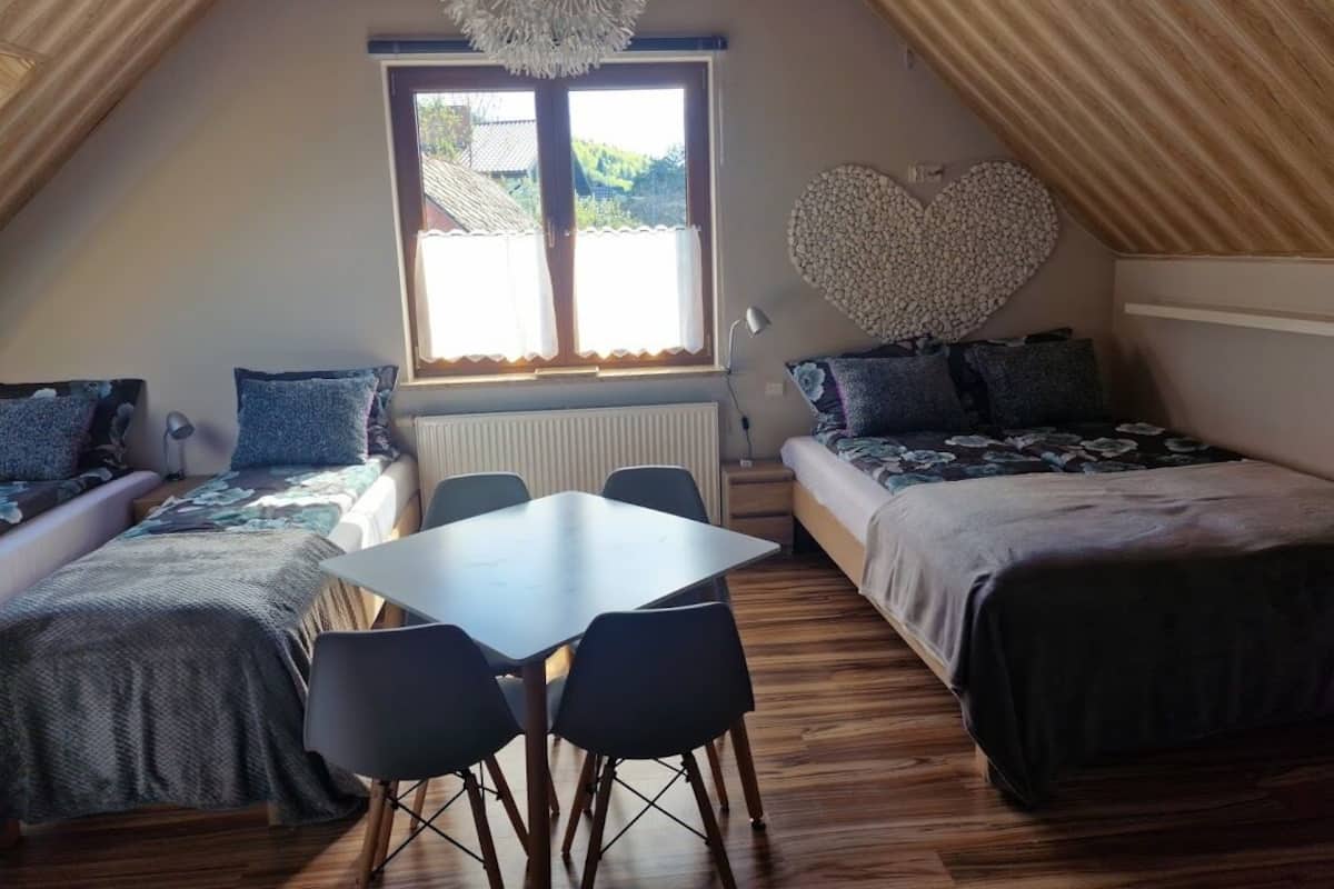A cozy attic bedroom with a loft bed, a dining table, and a heart-shaped wall decoration.